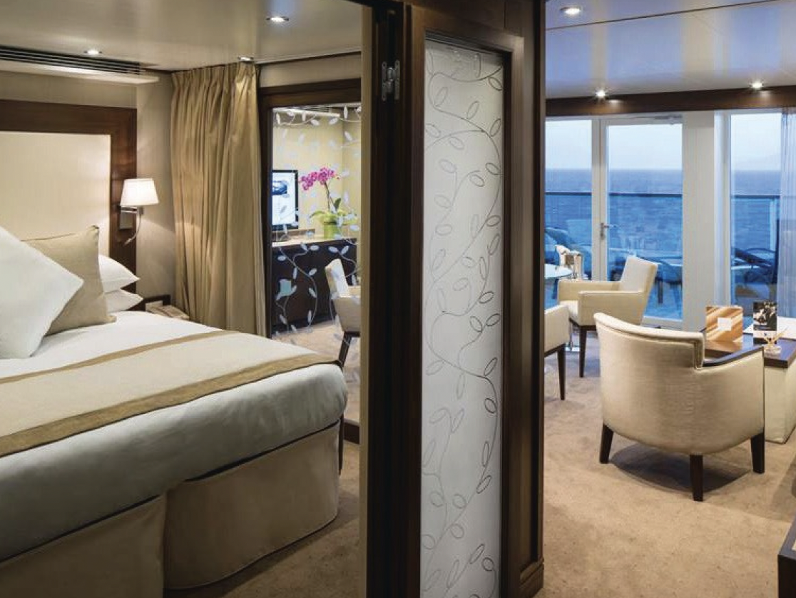 Luxury King Suite on an Alaskan Cruise. Big bed in the middle surrounded by bright lights with a view of the water.